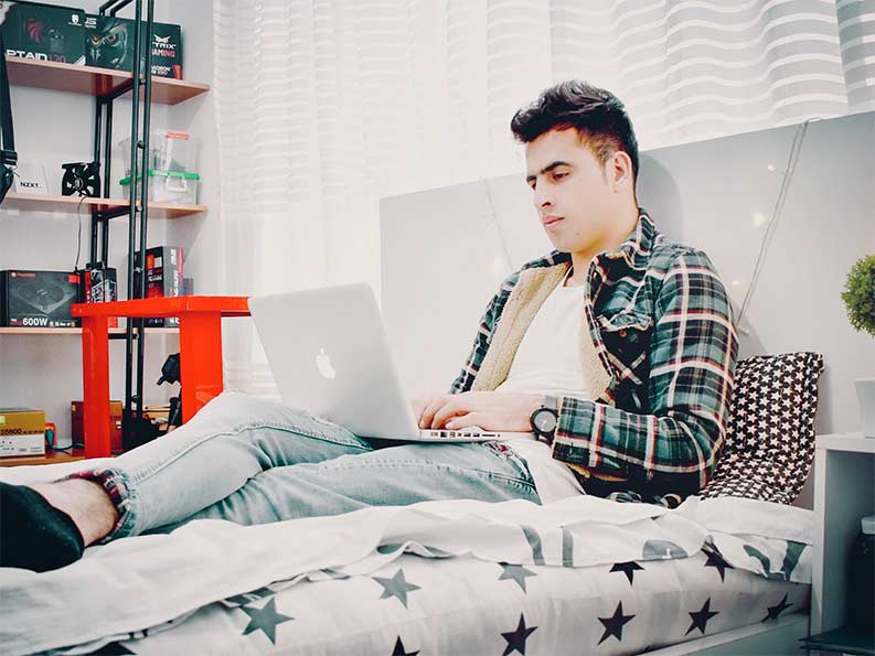 DIFC student lying on a bed on his laptop typing