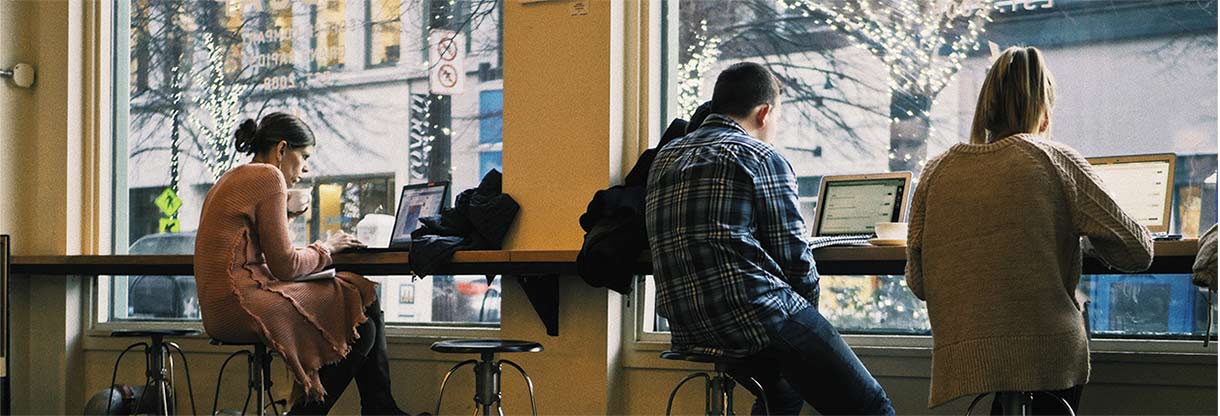 Students sitting at a desk on their laptops drinking coffee