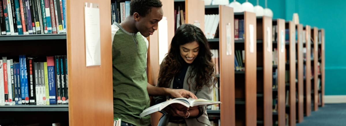 Two DIFC students in the library looking at a book