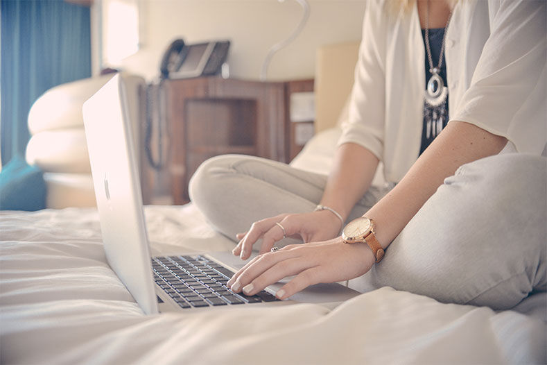 Female student sitting on a bed, typing on a laptop