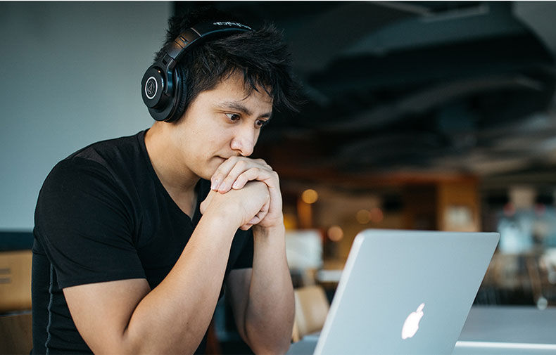 Malaysian student looking at a computer with headphones on