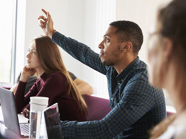 Students sitting at a desk, one with his hand up