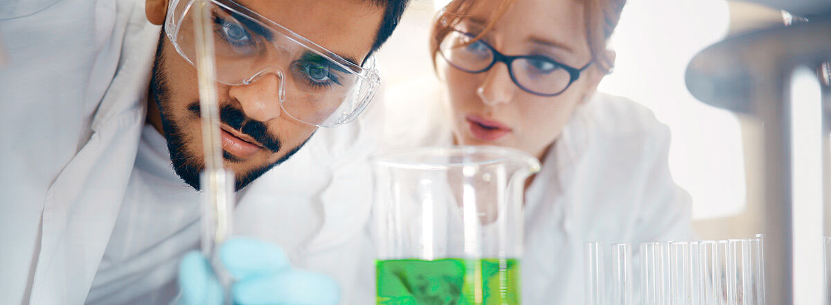 Two people in a lab wearing lab coats and safety googles