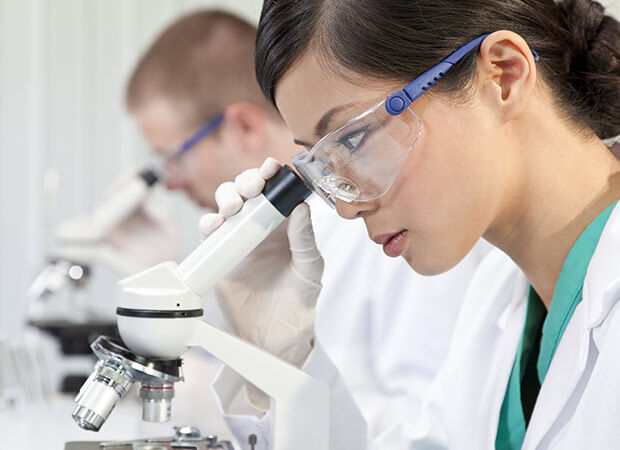 Malaysian female student wearing a lab coat and safety googles looking through a microscope